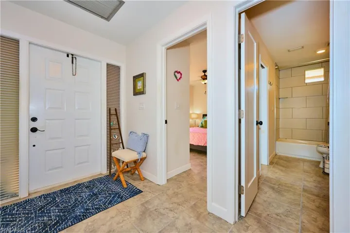 Entryway featuring a white paneled front door with sidelight windows, tile flooring, and a bath enclosure with horizontal tile wall surrounds