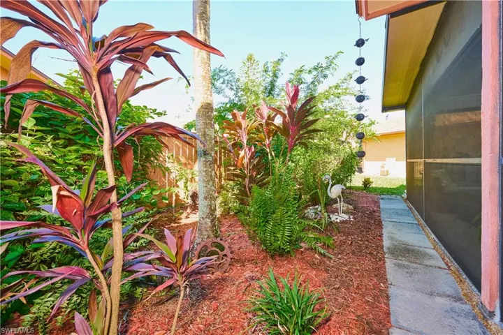 Landscaped garden featuring mature tropical plants, organic mulch beds, and a stone-paver walkway bordered by a screened-in structure