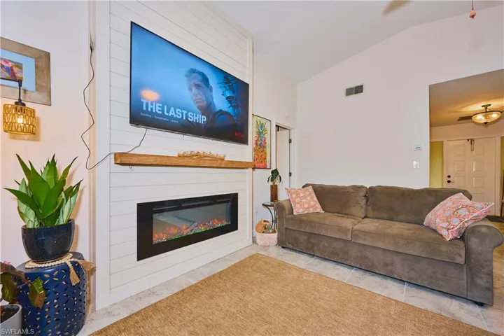 Floor-to-ceiling shiplap accent wall featuring an integrated electric fireplace and a wood-finish mantel, complemented by a vaulted ceiling