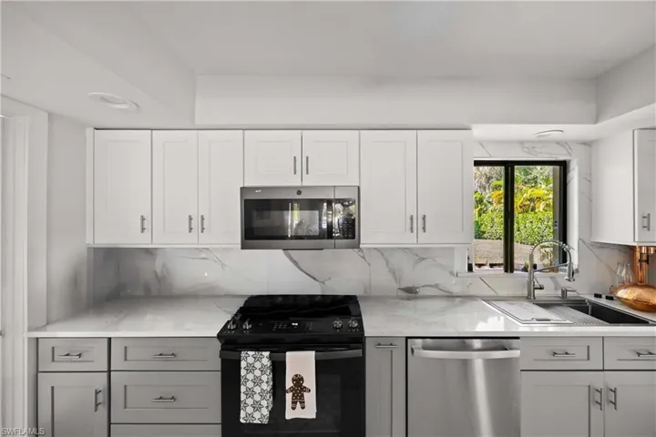 Kitchen featuring appliances with stainless steel finishes, white cabinetry, backsplash, and light stone counters