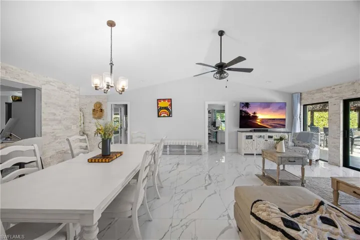 Dining area with light marble finish floors, an accent wall, a ceiling fan, lofted ceiling, and a chandelier