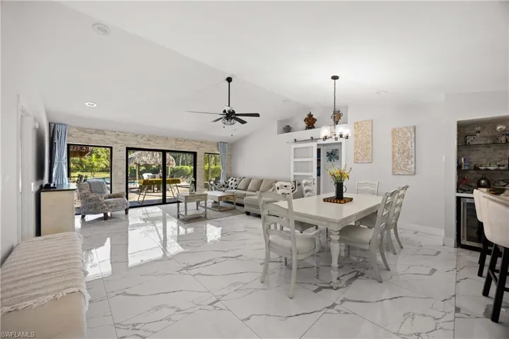 Dining area with light marble finish flooring, vaulted ceiling, a chandelier, ceiling fan, and beverage cooler