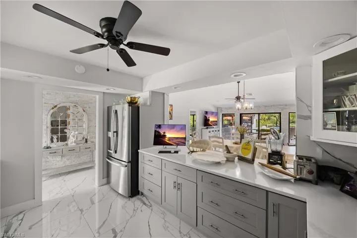Kitchen featuring stainless steel fridge, decorative light fixtures, light marble finish floors, ceiling fan, and a peninsula