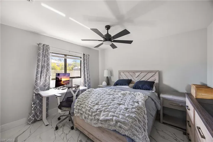 Bedroom featuring light marble finish floors, a ceiling fan, and a desk