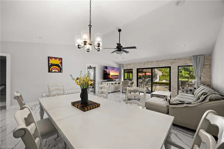 Dining area with light marble finish flooring, vaulted ceiling, a chandelier, a ceiling fan, and recessed lighting