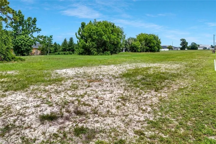 Expansive cleared lot featuring partial grassy coverage and a distant tree line