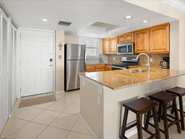 Kitchen with appliances with stainless steel finishes, light stone counters, a kitchen breakfast bar, light tile patterned floors, and a peninsula