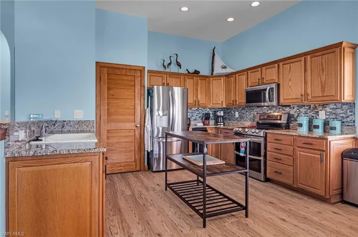 Kitchen featuring backsplash, stainless steel appliances, light wood-type flooring, and a sink