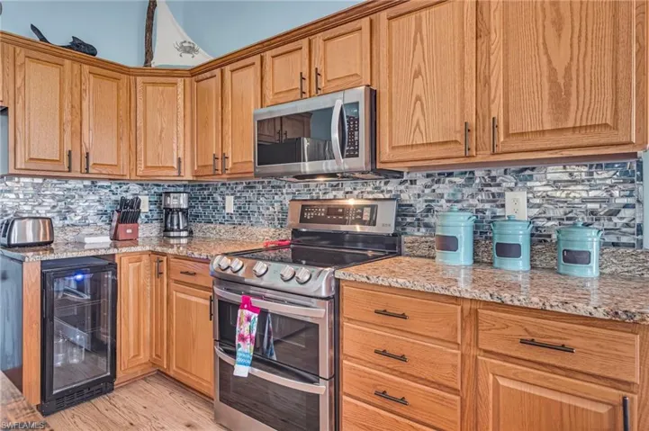Kitchen featuring light wood style finished floors, stainless steel appliances, wine cooler, light stone countertops, and decorative backsplash