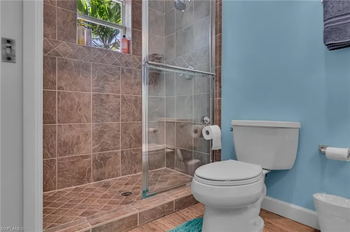 Bathroom featuring a shower stall, toilet, wood style finished floors, and baseboards