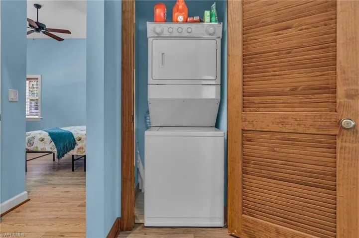 Laundry room featuring stacked washer / drying machine, baseboards, a ceiling fan, and wood stylefinished floors