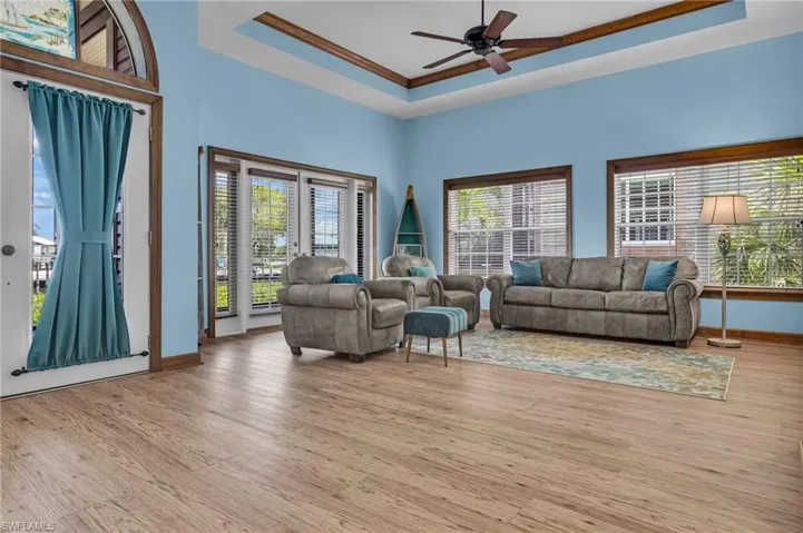 Living area featuring baseboards, a ceiling fan, light wood-type flooring, and a raised ceiling