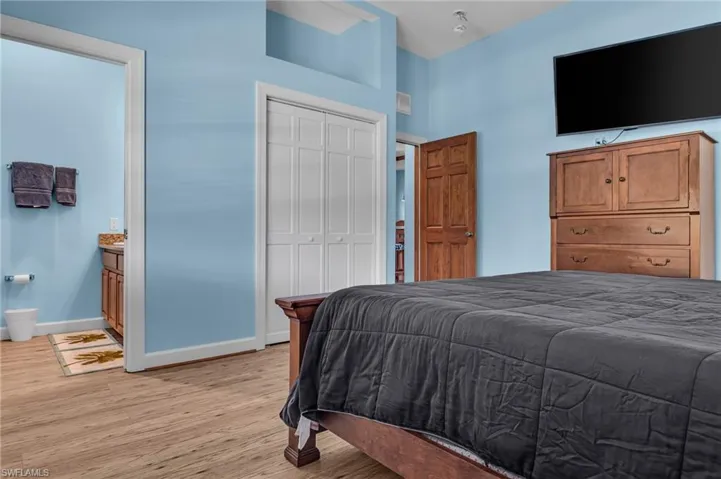 Bedroom with connected bathroom, baseboards, light wood-style flooring, and a closet
