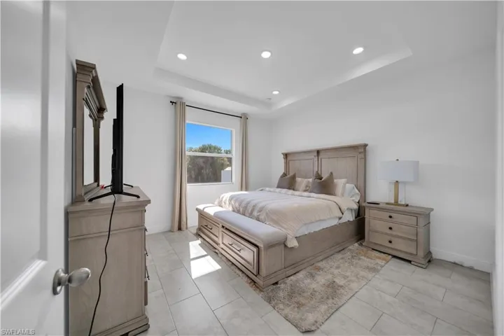 Spacious room featuring a tray ceiling with recessed lighting, an ample window, and light-toned tile flooring