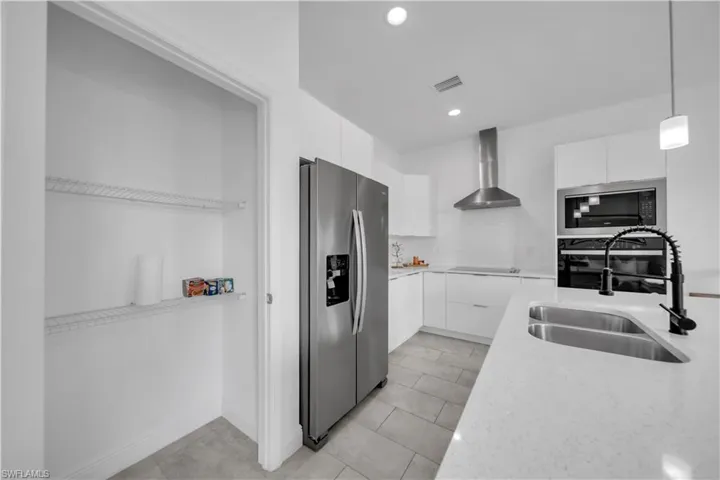 Modern kitchen featuring a large stainless steel refrigerator, white cabinetry, integrated oven and microwave, a stainless steel range hood, and a kitchen island with an undermount double-basin sink