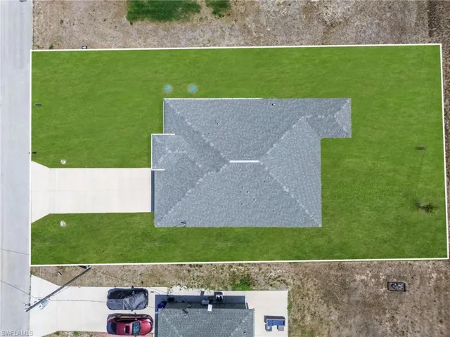 Expansive lot featuring a newly installed dark shingle roof, a generously sized concrete driveway, and a perimeter of vibrant green lawn