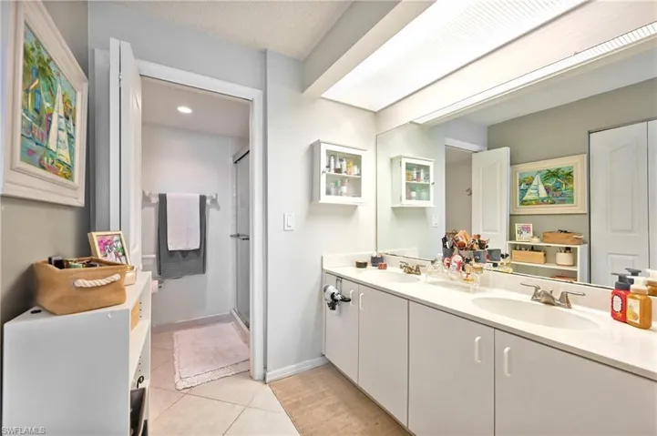 Full bath with double vanity, a shower stall, and light tile patterned floors