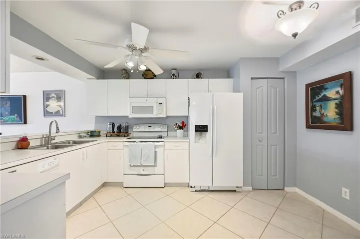 Kitchen with white appliances, a ceiling fan, light countertops, white cabinetry, and light tile patterned floors