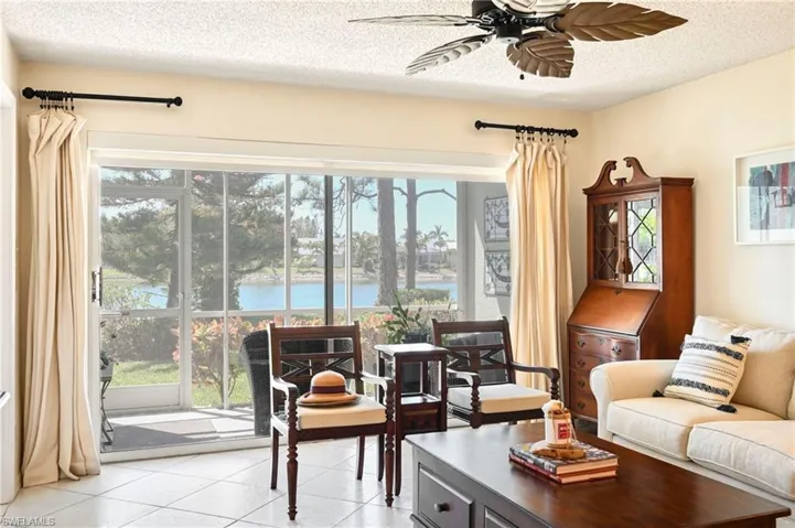 Living area with ceiling fan, a water view, light tile patterned floors, and a textured ceiling