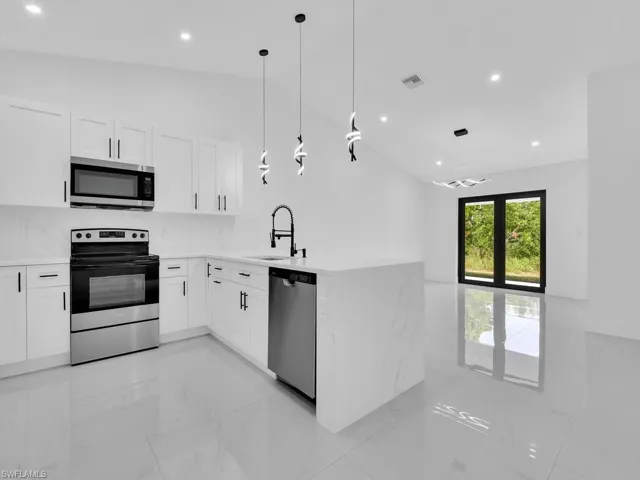 Kitchen with a peninsula, appliances with stainless steel finishes, light marble finish floors, hanging light fixtures, and white cabinets