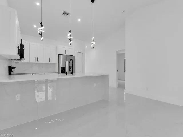 Kitchen with light stone counters, a peninsula, white cabinetry, stainless steel refrigerator with ice dispenser, and decorative light fixtures
