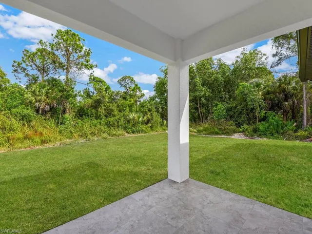 View of grassy yard with a patio area and view of scattered trees