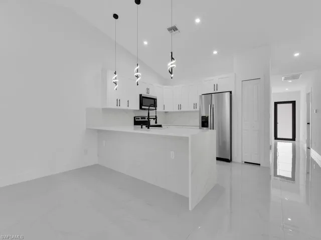 Kitchen with white cabinetry, pendant lighting, stainless steel appliances, a peninsula, and light stone counters