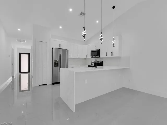 Kitchen with white cabinets, a peninsula, pendant lighting, stainless steel appliances, and light stone countertops
