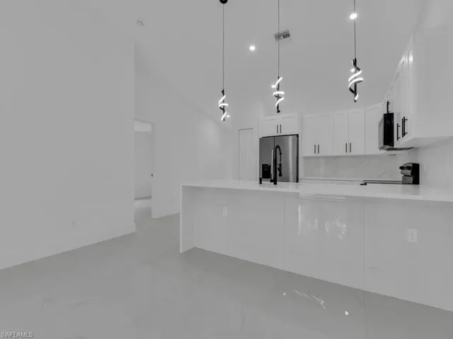 Kitchen featuring light stone counters, a peninsula, white cabinets, hanging light fixtures, and vaulted ceiling