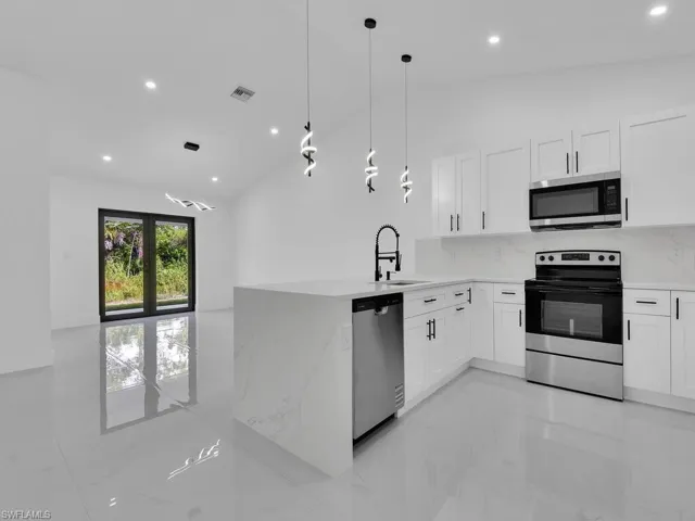 Kitchen featuring vaulted ceiling, appliances with stainless steel finishes, light marble finish flooring, backsplash, and a peninsula