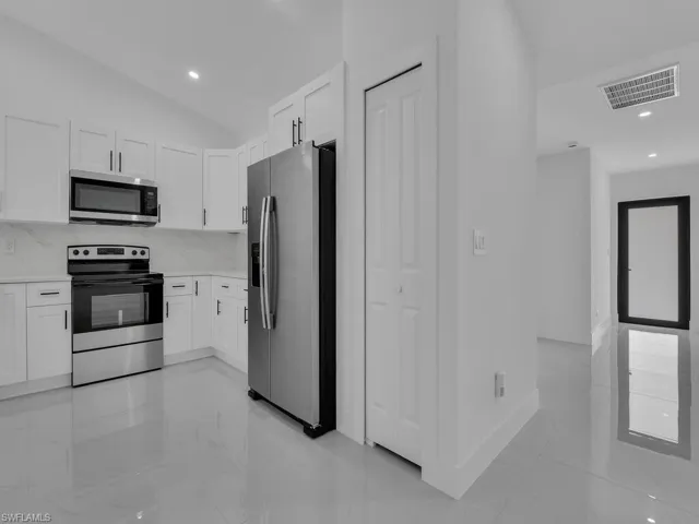 Kitchen featuring appliances with stainless steel finishes, white cabinets, backsplash, light marble finish flooring, and recessed lighting