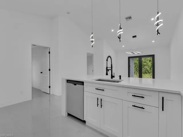 Kitchen featuring white cabinets, decorative light fixtures, stainless steel dishwasher, light stone counters, and light marble finish flooring