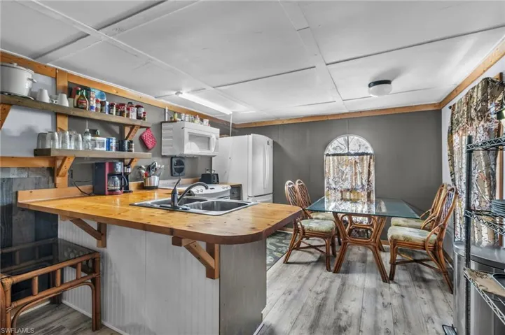 Kitchen featuring a sink, wood finished floors, white appliances, butcher block counters, and a breakfast bar area