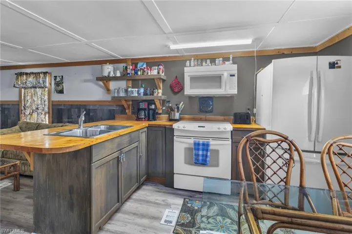 Kitchen with a sink, white appliances, open shelves, and butcher block counters