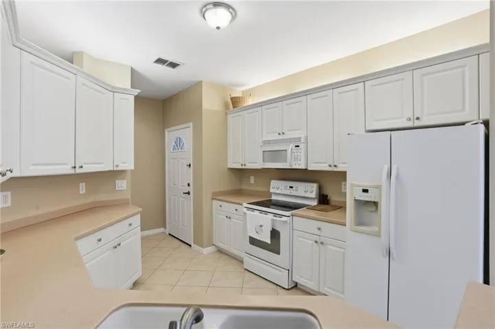 Kitchen featuring white appliances, light countertops, white cabinetry, and light tile patterned floors