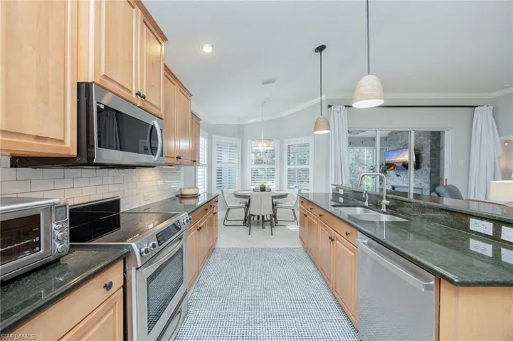 Kitchen with stainless steel appliances, crown molding, dark stone counters, pendant lighting, and tasteful backsplash