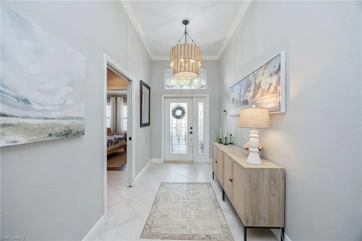 Entryway featuring a chandelier, ornamental molding, a textured wall, and light tile patterned flooring