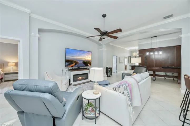 Living area with ornamental molding, ceiling fan, a glass covered fireplace, light tile patterned floors, and arched walkways