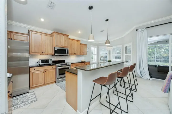 Kitchen featuring stainless steel appliances, ornamental molding, light tile patterned flooring, a kitchen bar, and dark stone counters