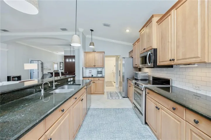Kitchen featuring lofted ceiling, backsplash, light wood finish cabinetry, stainless steel appliances, and dark stone countertops