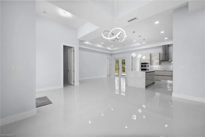 Unfurnished living room with a chandelier, recessed lighting, light tile patterned flooring, a tray ceiling, and french doors