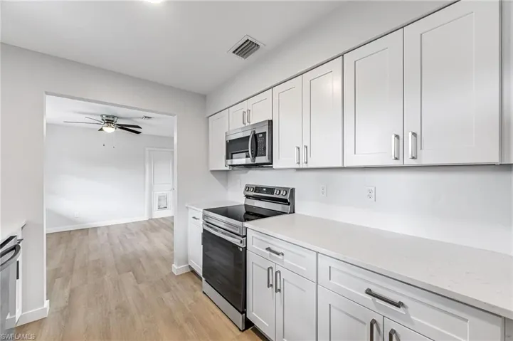 Kitchen with stainless steel appliances, white cabinets, light stone countertops, light wood-type flooring, and ceiling fan