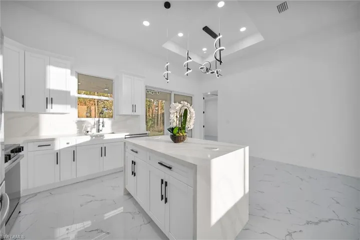 Kitchen featuring white cabinets, a kitchen island, light stone countertops, recessed lighting, and decorative light fixtures