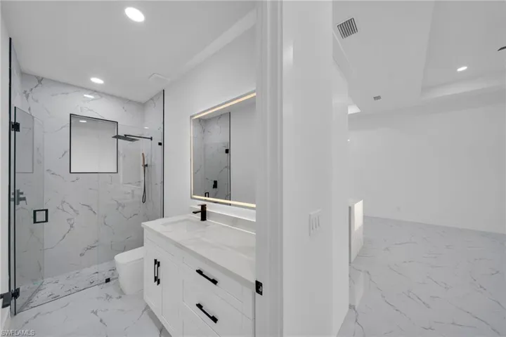 Full bathroom featuring recessed lighting, vanity, a marble finish shower, and light marble finish floors