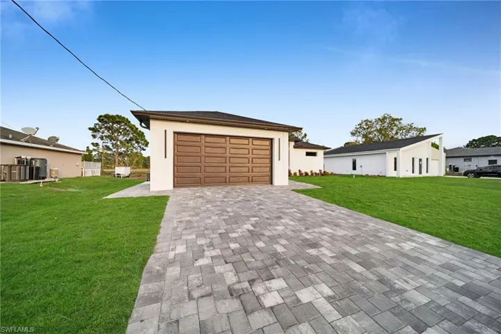 View of front of home with a front lawn, decorative driveway, a garage, and stucco siding