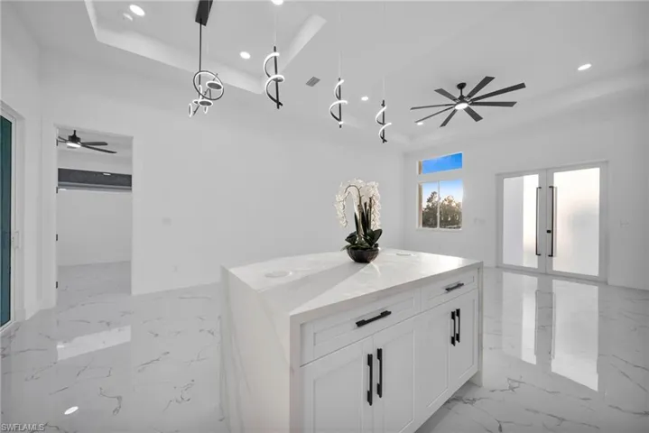 Kitchen with a ceiling fan, white cabinetry, open floor plan, a raised ceiling, and light stone counters