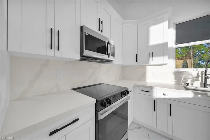 Kitchen featuring black electric range, stainless steel microwave, white cabinetry, and light stone countertops