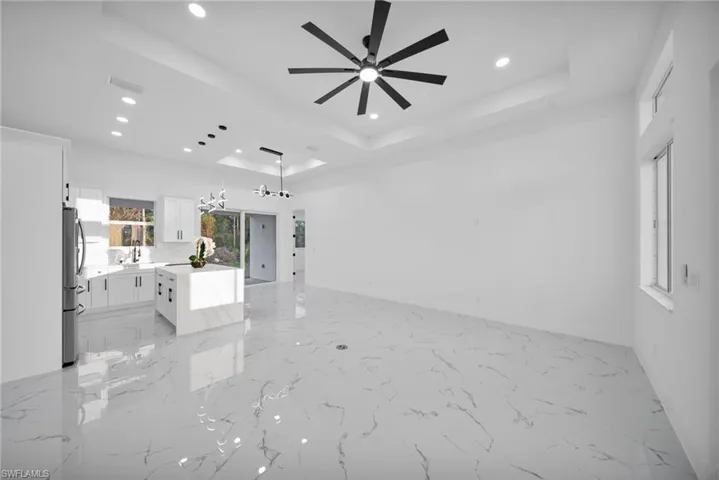 Unfurnished living room featuring a chandelier, light marble finish flooring, a tray ceiling, recessed lighting, and ceiling fan