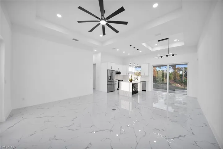 Unfurnished living room featuring a tray ceiling, recessed lighting, ceiling fan, light marble finish flooring, and a chandelier
