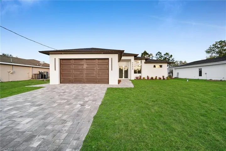 Prairie-style house with a front yard, decorative driveway, stucco siding, and an attached garage
